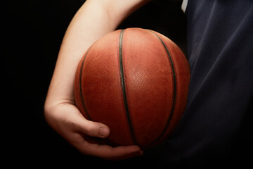 A hand holds a lit basketball near the hip on a black background, close-up, the start of the game,...