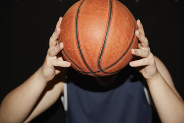 The hands of a basketball player hold the ball in front of them instead of the head on a black background, sports thinking, individual technique in basketball, basketball training