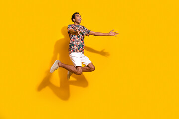 Fototapeta na wymiar Full length photo of friendly funny man wear print t-shirt jumping high holding arms empty space isolated yellow color background