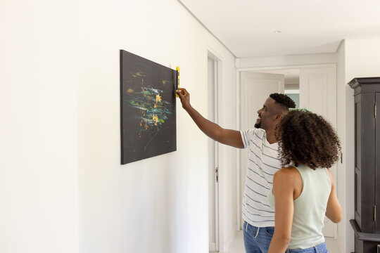 Biracial African American couple are hanging a painting at home with copy space