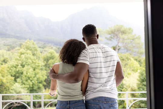 Biracial African American couple embrace, overlooking a mountainous landscape at home
