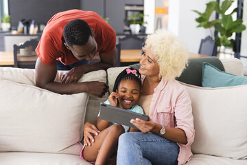 African American father and biracial mother are smiling at a tablet with an African American girl