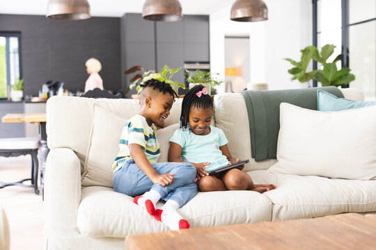 African American brother and sister are sharing a tablet on a sofa, smiling