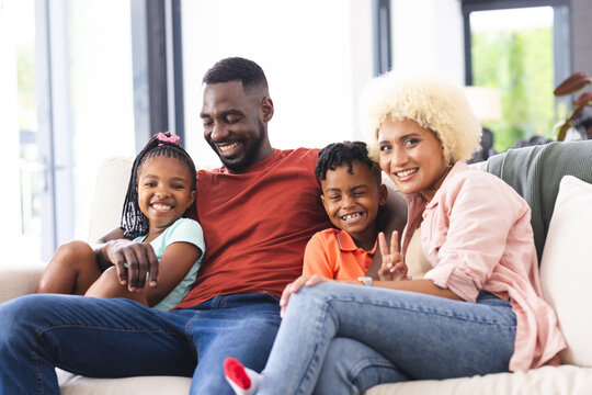 African American father, biracial mother, daughter, and son are smiling on a couch