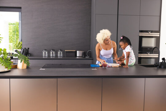 Young biracial mother prepares school lunch with African American daughter in a kitchen, with copy s