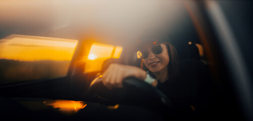 beautiful cool female driver in a baseball cap and sunglasses driving a car at sunset.