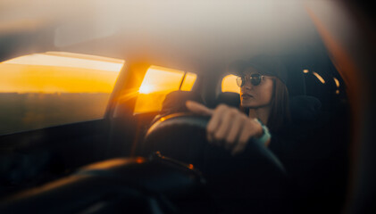 beautiful cool female driver in a baseball cap and sunglasses driving a car at sunset.