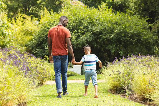 African American father and son walk hand in hand through a lush garden