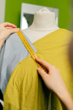 close up in a sewing workshop seamstress works with a mannequin on a blue fabric measures with a centimeter