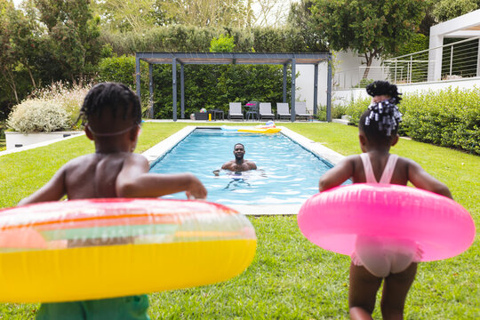 African American father swims in a pool while children with floaties watch