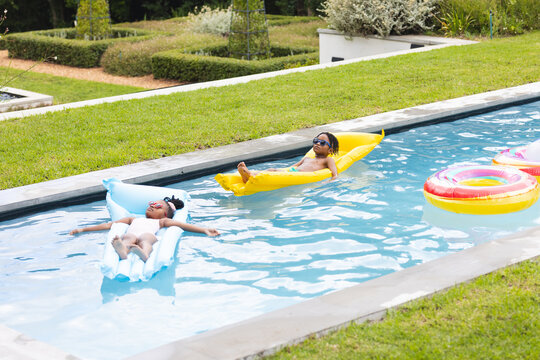 African American sister and brother enjoy floating in a pool on a sunny day