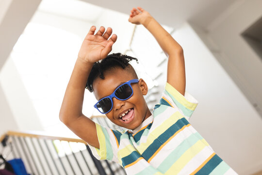 African American boy dances joyfully, wearing blue sunglasses and a striped shirt