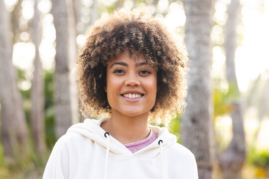 Young biracial woman smiles outdoors on a hike, surrounded by trees