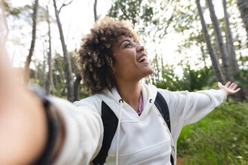 Young biracial woman with curly hair takes a selfie in the woods on a hike
