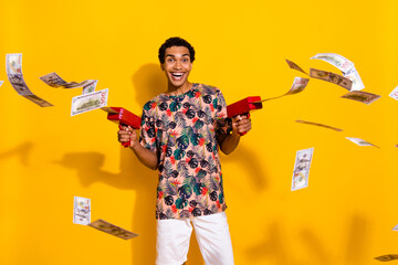 Photo of young crazy millionaire guy shooting money gun dollars banknotes thrown when chill at...