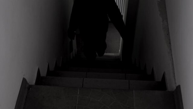 A scary amateur video of a man or a maniac with a knife, or an ax man climbing the steps in the dark. Horror, mysticism, crime, murderer.
