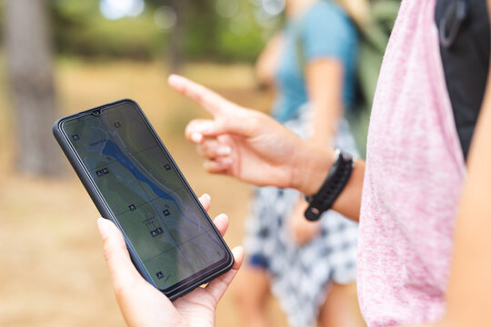 Person holds a smartphone displaying a map, pointing at the screen with another person in the backgr