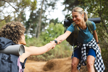 Young biracial woman helps a young Caucasian woman up a trail on a hike