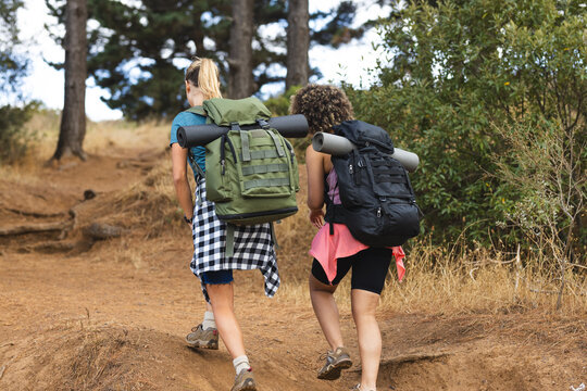 Young Caucasian woman and young biracial woman hike on a dirt trail on a hike