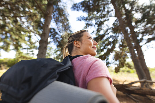 A young Caucasian woman with a backpack gazes into the distance on a hike