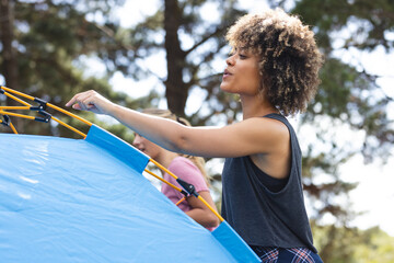 Young biracial woman with curly hair sets up a blue tent