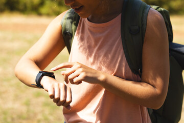 Young biracial woman checks her smartwatch outdoors on a hike