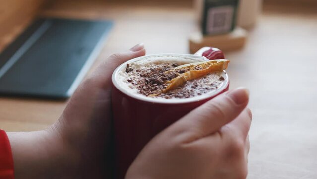 Coffee hot chocolate in female hands. Dried orange slice and grated chocolate.