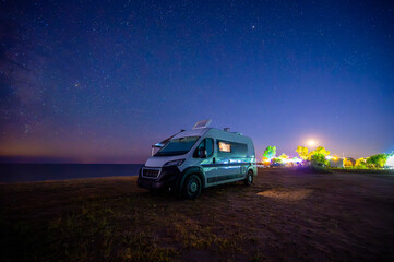 Fototapeta na wymiar Campervan or motorhome parked on the beach in Greece under the stars and milky way. Tourists enjoying and relaxing on the beach with RV campervan on family vacation.