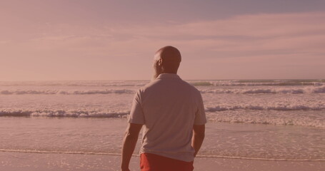 Rear view of african american senior man walking at the beach - Powered by Adobe