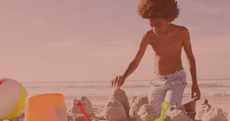 Naklejka premium African american young boy building sand castles at the beach