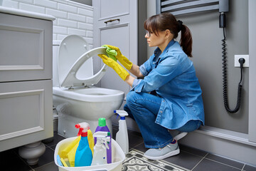 Woman in gloves using cleaning detergent clean toilet in bathroom