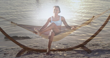 Image of light over happy african american woman in hammock on beach