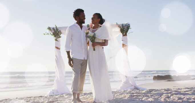 Image of dots over happy african american newly married couple on beach - Powered by Adobe