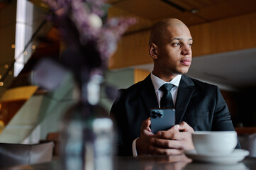 African american businessman in suit using smartphone near coffee in business center