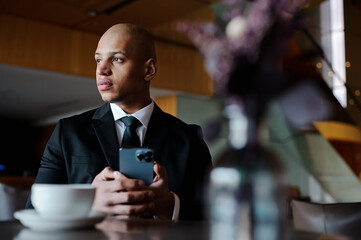 African american businessman using smartphone near blurred coffee in lobby of business center