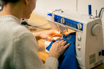 in a sewing workshop on a machine the seamstress master makes cut on a blue fabric
