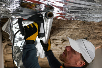 construction worker staples the vapor barrier to the ceiling