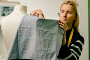 in sewing workshop seamstress works with a mannequin and pins blue fabric with a pin
