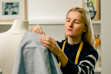 in sewing workshop seamstress works with a mannequin and pins blue fabric with a pin