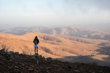 Una mujer visitando el mirador en Fuerteventura y disfrutando de la grandeza de las montañas áridas y bonitas - obrazy, fototapety, plakaty