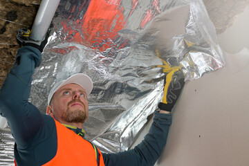 the construction worker holds a vapor barrier in his hand - preparation for fastening