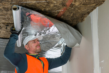 the construction worker holds a vapor barrier in his hand - preparation for fastening