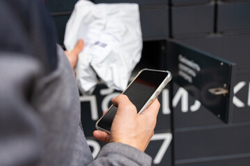 Man receiving parcel from automatic post box using smartphone outdoors. Modern delivery technologies concept.