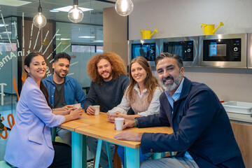 Colleagues gathered around a table enjoying coffee and conversation in a modern office kitchen. 