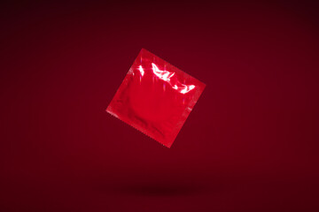 red condom floating in the air isolated on a red background, protection, contraceptive and safe sex concept, monochrome colours mock up