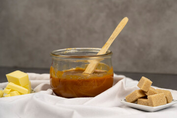 pot de caramel au beurre doux fais maison avec une petite cuillère en bois et du sucre roux