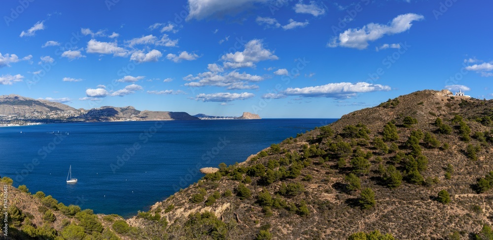 Sticker sailboat moored in a bay of the Serra Gelada Natural Park with the Albir Lighthouse in the background