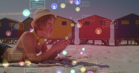 Image of social media icon over caucasian woman with phone on beach