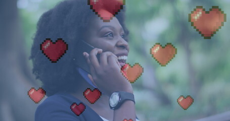 Image of heart icons over african american woman talking on smartphone