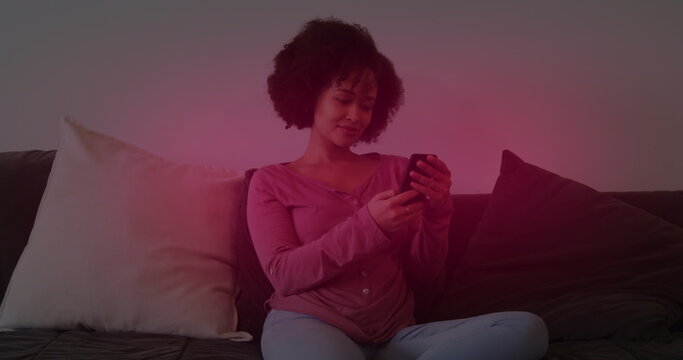 Young biracial woman with curly hair using a smartphone while sitting on a couch
